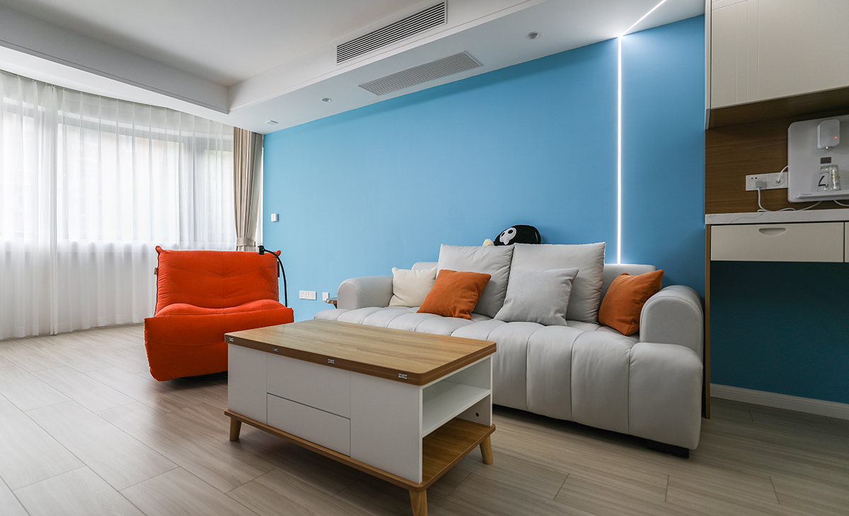  沙发背面采用小射灯把墙面照亮，天蓝色墙面配上低饱和奶茶色窗帘布，让整个空间活跃起来。