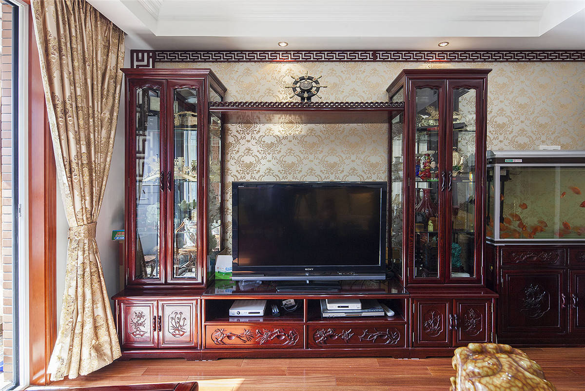 电视背景墙由传统的红木家具配上金色的墙纸，体现中式文化深沉、厚重的底蕴。

