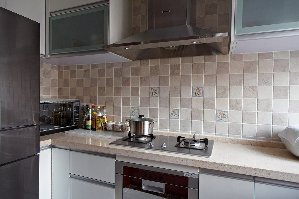 厨房运用错杂镶嵌的小花砖，但是整体橱柜运用整体统一的浅色色调，浅黄色的台面、现代简约的厨具表的得体大方。

