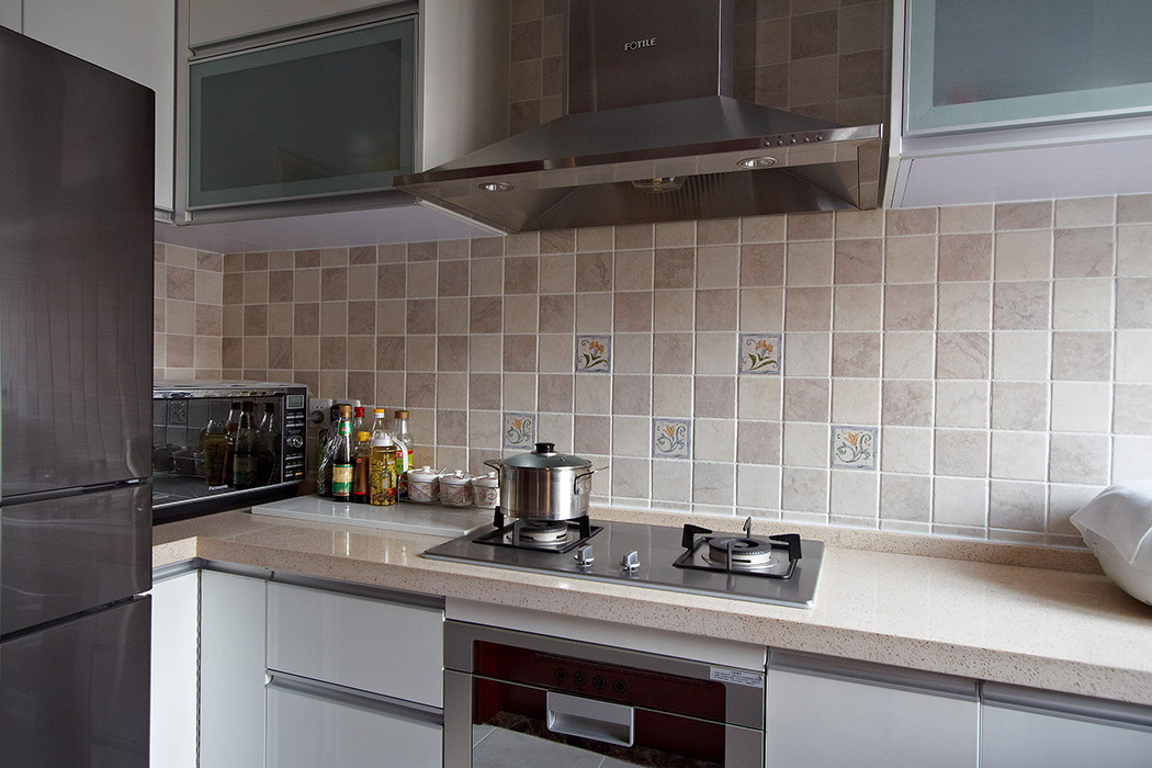 厨房运用错杂镶嵌的小花砖，但是整体橱柜运用整体统一的浅色色调，浅黄色的台面、现代简约的厨具表的得体大方。