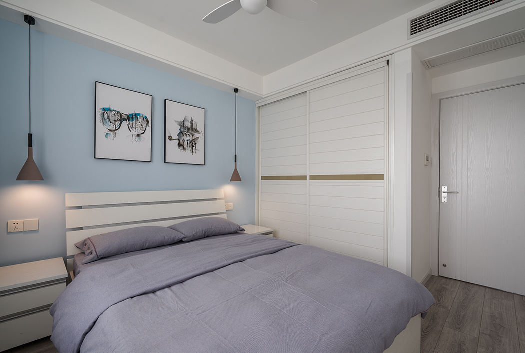  卧室爽朗大气的线条勾勒出干练的个性气息，为了不打破安逸舒适的空间感，陶瓷色的床头灯与蓝灰色的布艺窗帘恰到好处的降低空间过于高调活跃的色彩基调，同时衬托富有质感的装饰画，浅紫色软麻布床单搭配出丰富的层次感，传递专属现代主义的奢华、温馨、向往自由的风格，舒缓了人的紧张心情，让人坦然释放，回归自我。
