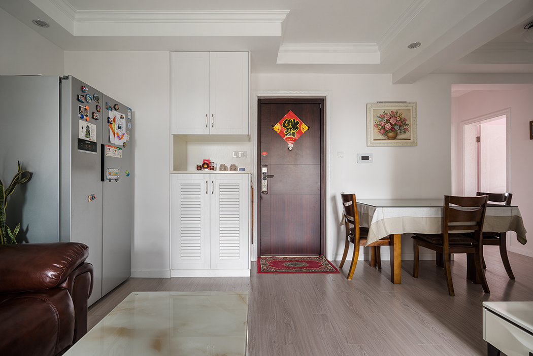 空间从色彩到材质到家具的选择，尽显简约与舒适气息。整个空间以亮色为主色调，现代的硬朗线条和皮质沙发的组合，有种现代线条感。入户简约鞋柜与双开门冰箱组合增添几分欢快与质感。
