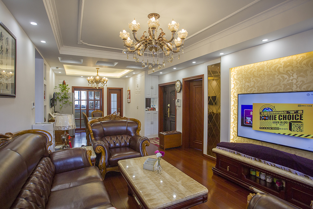 客厅整体风格都是一种中式和欧式混搭的效果，中式的柚木色的地板和木门以及中国字画，再配以欧式的皮沙发，水晶吊灯，无处不显示欧式和中式的碰撞。
