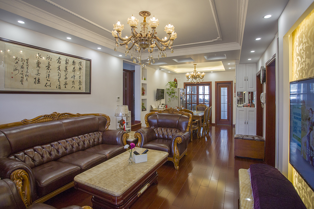 客厅整体风格都是一种中式和欧式混搭的效果，中式的柚木色的地板和木门以及中国字画，再配以欧式的皮沙发，水晶吊灯，无处不显示欧式和中式的碰撞。
