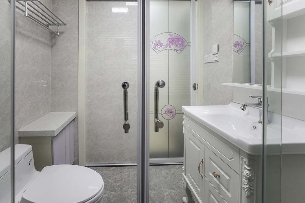 卫生间主要以实用为主，材质上要尽量干净、清爽，方便打理，颜色上不能花哨，本案卫生间设计以白色的铝合金集成扣板、灰色的墙地砖、白色的洁具搭配，既统一协调，又不单调呆板。淋浴房、浴室柜、杂物柜和坐便器布置的恰到好处，使不大的卫生间空间充分利用，进门后所有的实用功能一览无余地展现在主人的面前，让主人对空间的使用更方便。
