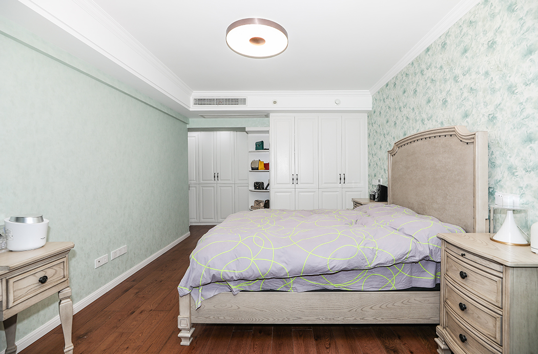 淡蓝色花纹墙纸搭配白色的踢脚线跟衣帽柜，提亮整个空间。高大的实木床，对称的床头柜，现代美式风格尽显。
