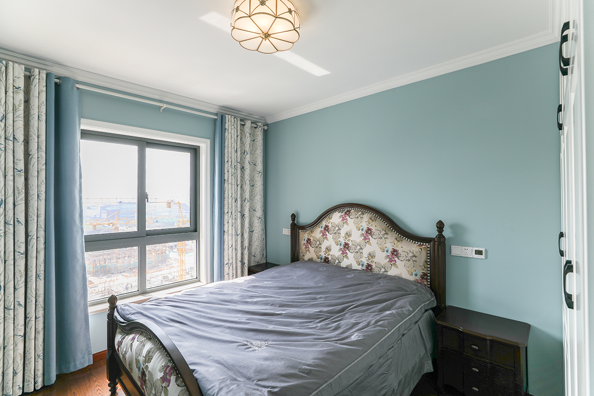 客厅采用了暖色调，所以在卧室上更改了客户喜欢的蓝灰色，碎花的窗帘和美式碎花的床背靠，和客厅成了不一样的对比色。
