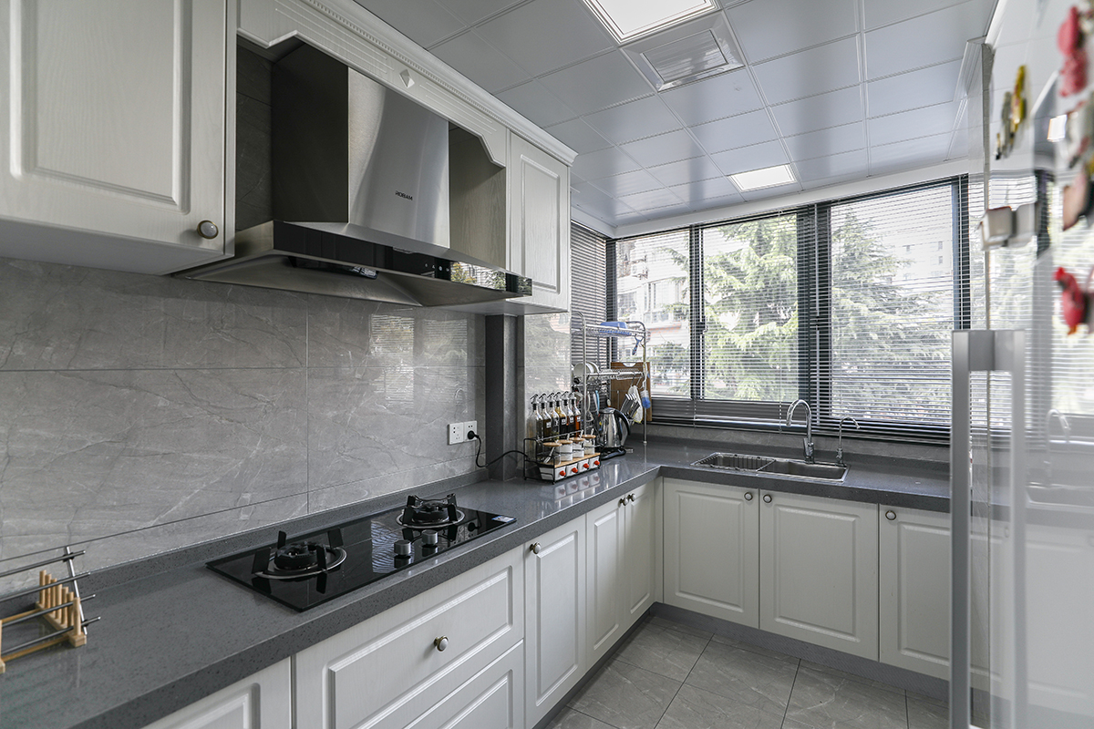 原本狭小的厨房和工作阳台打通之后，变得宽敞明亮，整体使用灰色的玻化砖，大气时尚，又和深灰色台面相呼应，同时和白色模压门板的橱柜形成对比。
